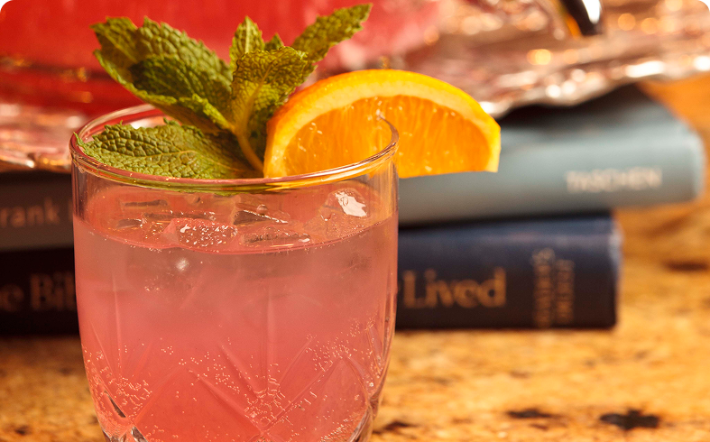 Pink drink with orange and mint garnish.